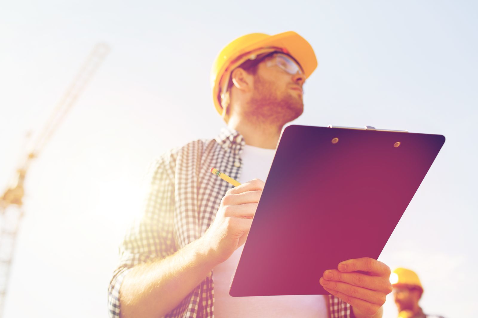 An adjuster in a hard hat writing on a clipboard at a job site