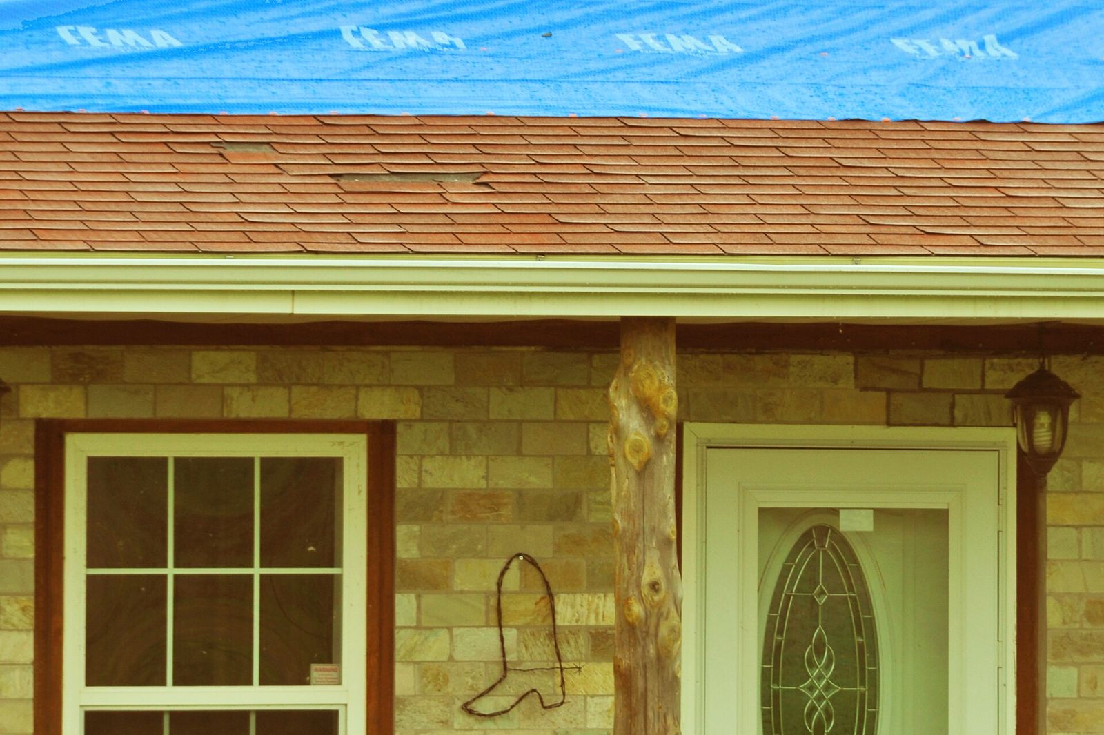 Blue tarp over the ridge of a storm-damaged shingle roof